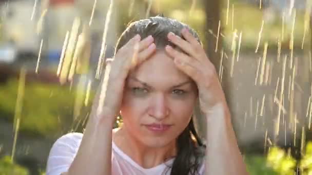 La joven sonríe y ríe bajo la lluvia. Las gotas de lluvia caen sobre su rostro y ella es feliz con la vida y la naturaleza alrededor. Concepto de Naturaleza y Felicidad Vida, Aventura, Pureza — Vídeo de stock