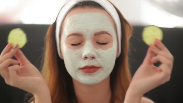 Close Up of a Girl With a Mask On Her Face And a Towel On Her Head That Closes Her Eyes With Cucumbers And Smiles. Woman Wearing Face Mask. Face Care Concept — Stock Video