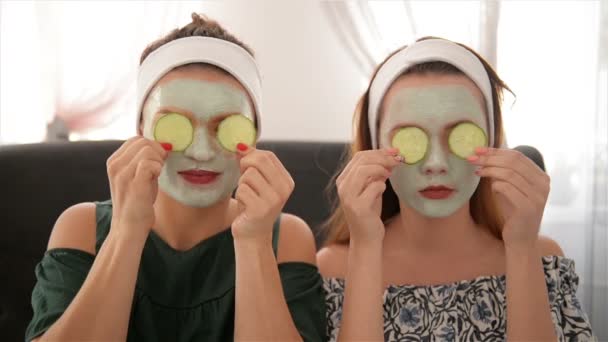 Twee glimlachende vrouwen die komkommers houden. Portret van meisjes in de spa salon. Health Beauty concept, gezichtsmasker, samen. — Stockvideo