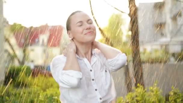 Hermosa mujer con el pelo mojado disfrutando de la lluvia y mirando hacia el cielo. Pretty Woman in Summer Garden Tener un montón de diversión. Feliz día lluvioso. Vídeo colorido en colores cálidos. Hojas con gotas de lluvia . — Vídeos de Stock