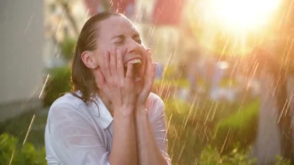 Vacker kvinna med vått hår njuter av regnet och blickar upp mot himlen. Vacker kvinna i sommarträdgården har mycket roligt. Lycklig regnig dag. Färgglad video i varma färger. Löv med regndroppar. — Stockvideo