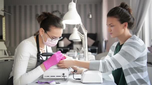 Una mano de manicura con clavos se encuentra en la mano de una manicurista en un guante higiénico rosa. Maestro hace manicura francesa clásica . — Vídeo de stock