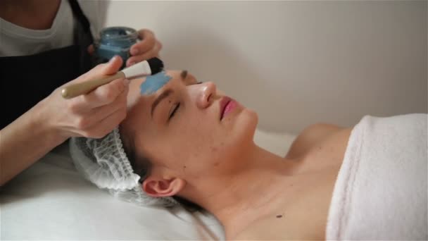 Cosmetoloog maakt de procedure voor het reinigen en hydrateren van de huid. Masker met speciale borstel aan het gezicht van de vrouw toe te passen. Jong meisje zorgt voor haar huid. Bezoeken cosmetologie kliniek. Aethetische geneeskunde. — Stockvideo