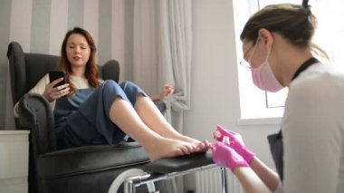 Güçlü Salon Çalışanı. Müşteri Telefonda Konuşurken Lüks Güzellik Salonunda Kür Masajı ile Pembe Kauçuk Eldiven İşleme Bacaklar Konsantre Master.