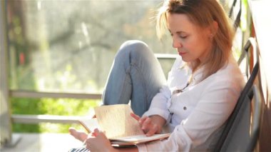 Güneşli bir günde, terasta ilginç bir kitap okuyan genç ve güzel bir kadın..