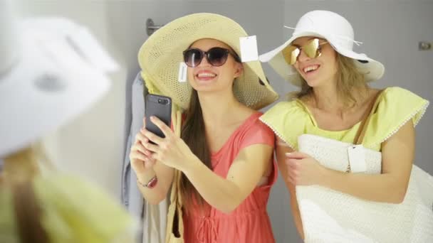 Mulher feliz tentando um novo óculos de sol no guarda-roupa na loja de roupas. Amigos femininos se divertindo roupas de compras. Senhoras fazendo espelho Selfie no quarto de montagem . — Vídeo de Stock