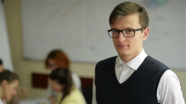 Primer plano del joven trabajador guapo que usa anteojos y camisa de franela en una pequeña oficina con otro personal en segundo plano — Vídeos de Stock