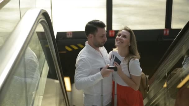Hombre abrazando a la mujer mientras se ubica en las escaleras móviles. Llevan equipaje. Pareja durante el concepto de viaje — Vídeo de stock