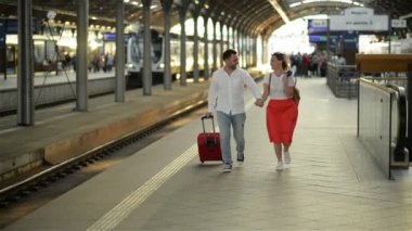 Tren istasyonunda bavulu olan bir çift koşuşturuyor. Elinde Pasaport Tutan Kadın.