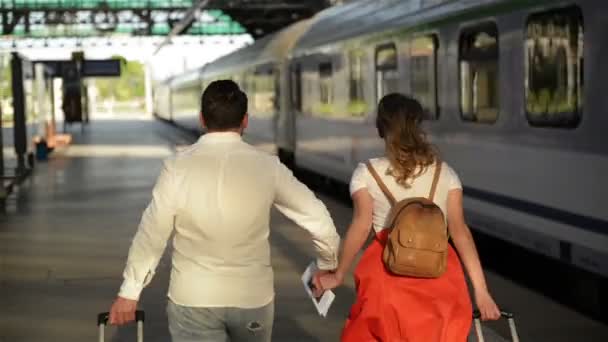 Running paar met een koffer in een trein station. Vrouw die paspoorten in haar handen houdt terwijl de trein vertrekt. — Stockvideo