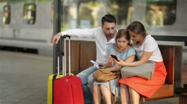 Sevimli Kızı Olan Anne ve Baba, Tren İstasyonu'nun veya Havaalanı'nın bekleme odasında oturuyorlar. Güzel Anne Telefonunu Gösteriyor. Çocuklar Akıllı Telefona Bakıyor.