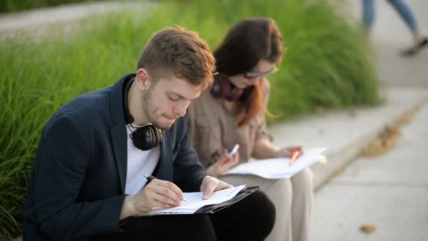 Couple attrayant d'hommes et de femmes assis sur des escaliers dans le centre-ville urbain dans le style d'affaires décontracté intelligent travaillant ensemble sur le projet, souriant, personnes indépendantes élégantes tenant des carnets, écrivant . — Video