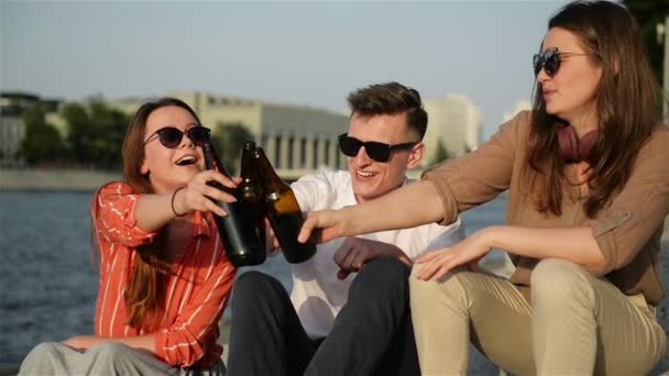 Un grupo de estudiantes divirtiéndose al aire libre. Están bebiendo cerveza, hablando entre ellos y riéndose. Tiempo de verano se ve muy bien en segundo plano . — Vídeo de stock