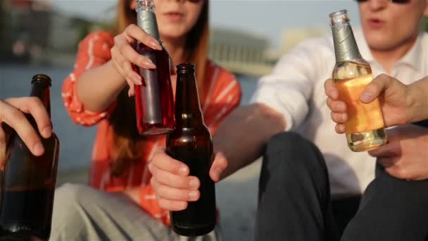 Vista de cerca de los estudiantes clinking botellas con una cerveza artesanal. Jóvenes divirtiéndose juntos. Pasar tiempo al aire libre. Concepto de vacaciones y verano . — Vídeo de stock