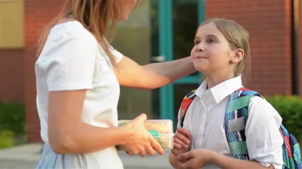 Onderwijs, familie en zorg concept. Liefdevolle moeder geven dochter school lunch in de buurt van de school. — Stockvideo