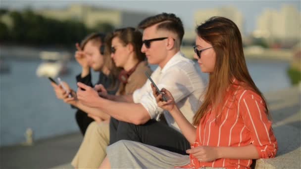 Quatre amis riant heureux et regardant les médias sociaux dans un téléphone intelligent dans la rue. Tout le monde avec son propre téléphone. Meilleurs amis et étudiants passent du temps ensemble à l'extérieur . — Video