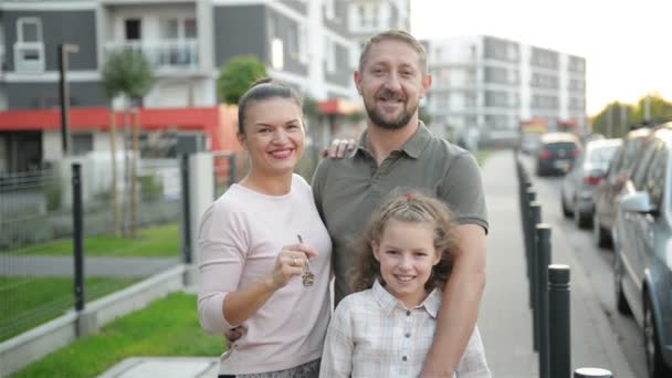 Familia feliz con los cabritos que sostienen al aire libre llaves de la casa de campo grande. Dueños de bienes raíces de lujo sonrientes Pareja e hijos abrazando en la calle después de comprar una casa nueva. Concepto de préstamo hipotecario . — Vídeos de Stock