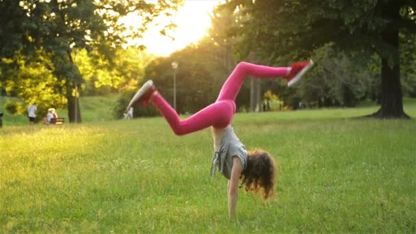 Happy Little Girl In Dress Is Jumping On Park Meadow And Making Acrobatic Wheel. Summer Outdoor Activities. Slow Motion. — Stock Video