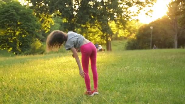 Niña divirtiéndose en la hierba verde mientras hace una rueda acrobática. Joven chico deportivo tiene un muy buen estado de ánimo . — Vídeos de Stock