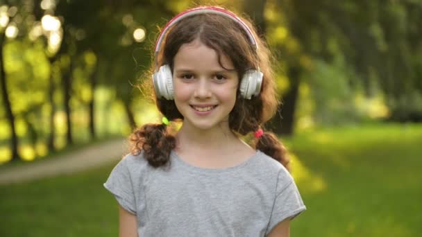 Portrét přitažlivé kavkazské malé studentky s krásnými hnědýma očima se sluchátky. Šťastné usmívající se dítě pohled na kameru. — Stock video
