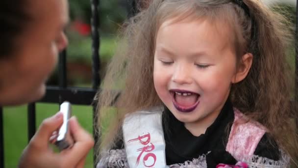 Glad halloween. Attraktiv ung kvinna med sin lilla söta dotter förbereder sig för att Halloween utomhus.. Mamma med dotter har roligt medan du gör Halloween katt makeup. — Stockvideo