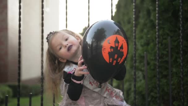 Liten flicka i prinsessan kostym håller en svart ballong. Hon ser väldigt glad för idag är Halloween semester. — Stockvideo