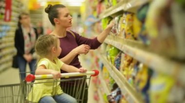 Anne ve kızı süpermarkette alışveriş. Kahvaltı gevreği satın alıyor. Bir süpermarket arabası içinde oturan bir kızı.