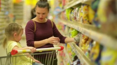 Anne ve kızı süpermarkette alışveriş. Kahvaltı gevreği satın alıyor. Bir süpermarket arabası içinde oturan bir kızı.