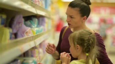 Süpermarket arabası içinde oturan lolipop tatlı kız. Anne arka plan üzerinde ıslak mendil seçer.