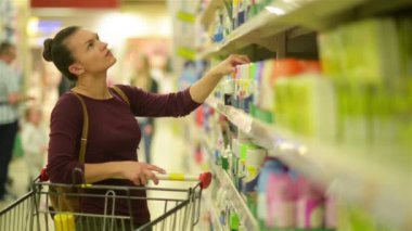 Genç kadınlar mendil süpermarket başlangıç rafı seçer. Beyaz görünüm bir kızla süpermarkette alışveriş yapar. HD, arabası, öğeleri, süpermarket iç.