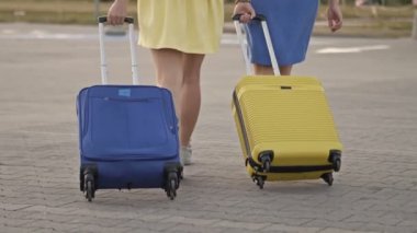 Tren istasyonunun platformunda yürüyen bavullu yolcular. Bagajı olan iki kadın havaalanına gidiyor