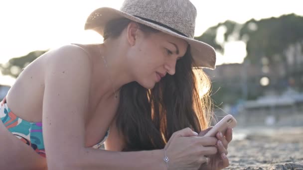 Perfil de una mujer que envía mensajes de texto en un teléfono inteligente en la playa con el mar al fondo — Vídeo de stock