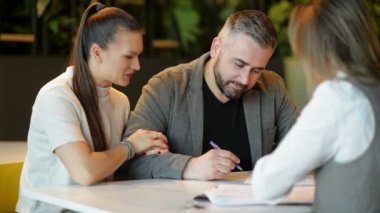 Emlakçı ve Genç Çift Ofis Masası'nda Oturan Side View Satılık Emlak Tartışıyor. Mutlu Çift Ev Sahibi Oldu.