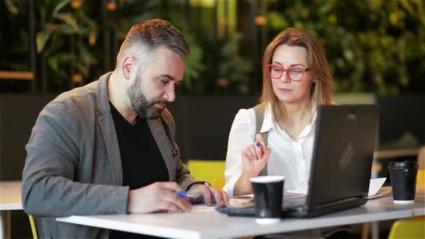 Paar medewerkers die samenwerken op kantoor. Twee zakelijke werknemer voorbereiden van nieuw project op laptop. Ze schrijven de details in een notebook. — Stockvideo