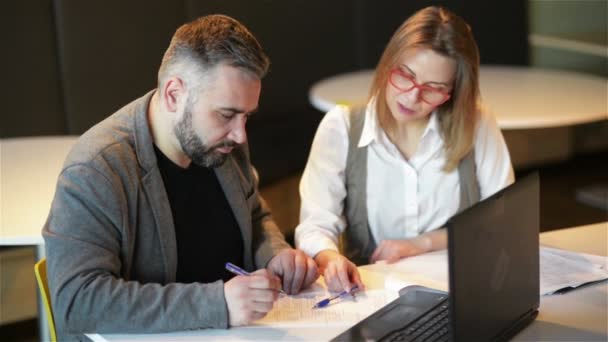 Couple de collègues travaillant ensemble au bureau. Deux travailleurs d’affaires préparant le nouveau projet sur l’ordinateur portatif. Ils écrivent les détails dans un cahier. — Video