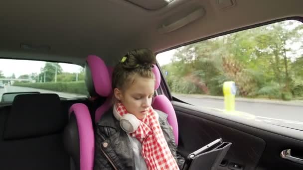 Chica adolescente con auriculares sentados en el asiento del coche y el uso de la tableta digital durante el viaje — Vídeos de Stock