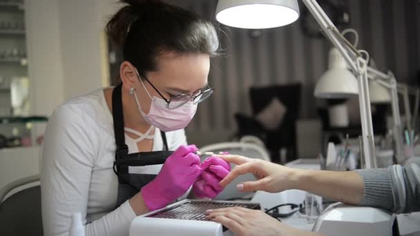 Een manicure hand met nagel ligt aan de hand van een Manicurist in een roze hygiënische handschoenen. Master doet klassieke French manicure. — Stockvideo