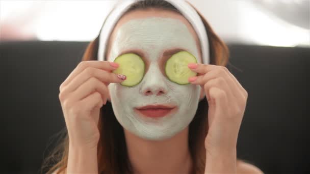 Close Up of a Girl With a Mask On Her Face And a Towel On Her Head That Closes Her Eyes With Cucumbers And Smiles. Woman Wearing Face Mask. Face Care Concept — Stock Video