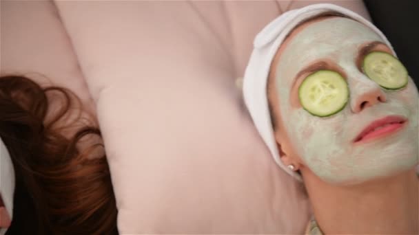 Home Spa. Drie vrouwen houden stukjes komkommer op hun gezichten liggend op het bed. Schoonheids salon concept, gezondheid. — Stockvideo