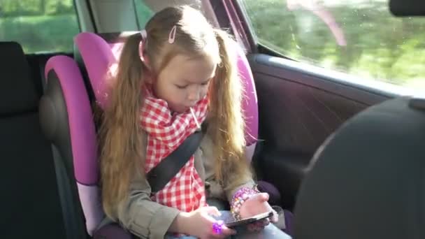 Young girl using smartphone in the car. Cute teenage girl playing on smartphone, while riding drive on the back seat. Travel concept — Stock Video