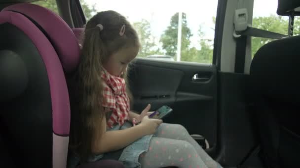 Chica joven usando el teléfono inteligente en el coche. Linda adolescente jugando en el teléfono inteligente, mientras conduce en el asiento trasero. Concepto de viaje — Vídeos de Stock