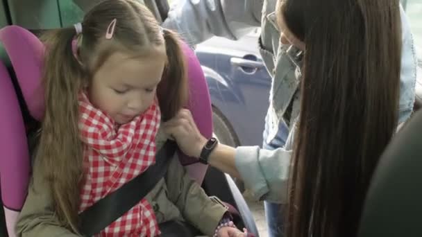 Vacker omtänksam mor fastsättning flicka med säkerhetsbälte i baksätet på bilen medan familjen ska på semester road trip. Barnet spänns fast i bilen under resan. — Stockvideo