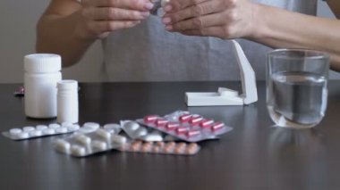Kadın ilaç alıyor ve ilaç kesicisi kullanıyor. Baş ağrısı ve ateş için ilaç alıyor, baş ağrısını tedavi ediyor.