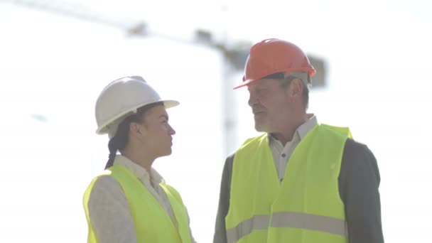 Två byggare, en man och en ung kvinna, diskuterar arbetsfrågor. Mot bakgrund av en kran. — Stockvideo