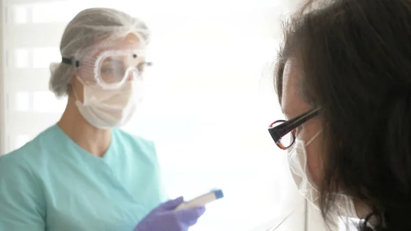 Verpleegster in medisch masker, bril en handschoenen meet de temperatuur van de patiënt met een contactloze infrarood thermometer. Stockfoto