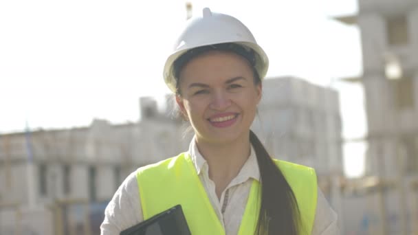建筑工地的女建筑工人穿着防护服。女孩拿着装有文件和微笑的文件夹. — 图库视频影像