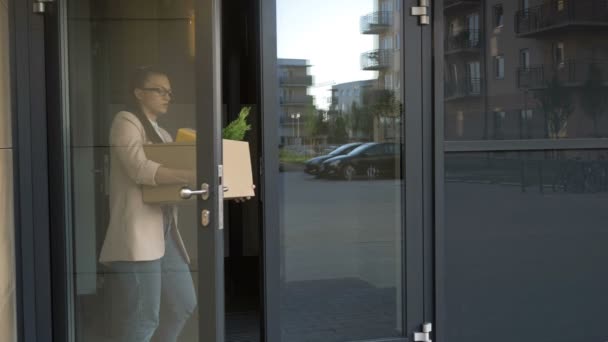 Una joven triste que acaba de perder su trabajo sale por la puerta de la oficina. En sus manos hay una caja con pertenencias personales. Crisis económica . — Vídeos de Stock