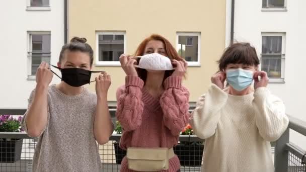 Ende der Covid-19-Pandemie. Drei Frauen, die auf dem Balkon stehen, ziehen medizinische Masken ab. Sie lächeln freudig und winken mit den Händen. — Stockvideo