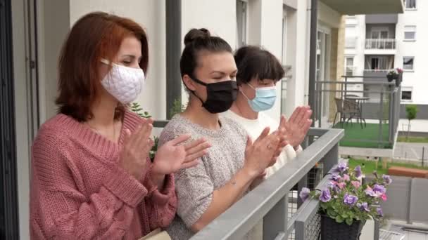 Lidé se radují na konci epidemie koronaviru. Tři ženy v lékařských maskách, stojící na balkóně činžovního domu, vesele tleskají. — Stock video