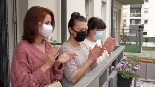 Folk gläds i slutet av coronavirusepidemin. Tre kvinnor i medicinska masker, stående på balkongen i en lägenhetsbyggnad, glatt applådera. — Stockvideo